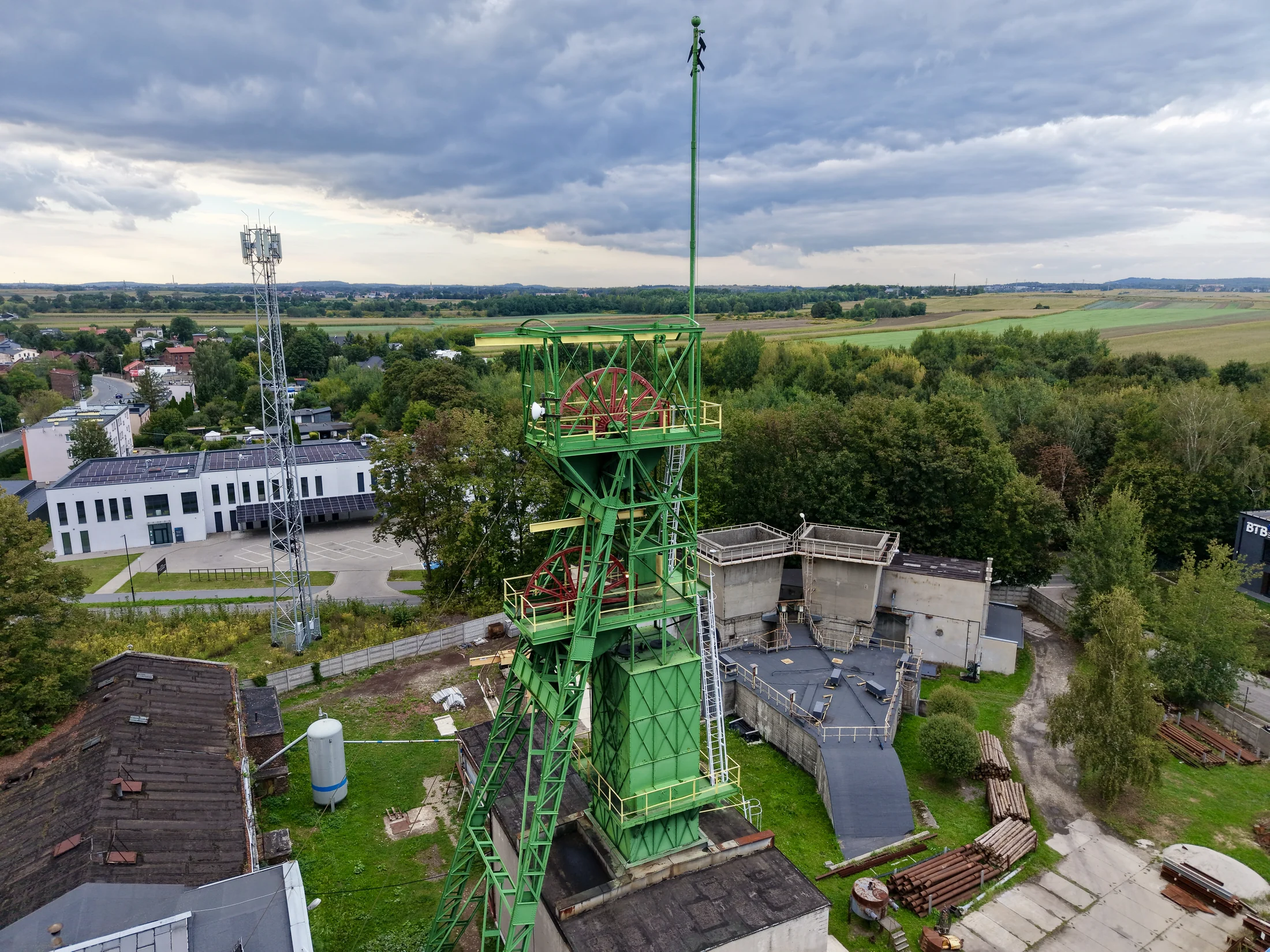Wysoka zielona konstrukcja przemysłowa na tle budynków, drzew i pól.
