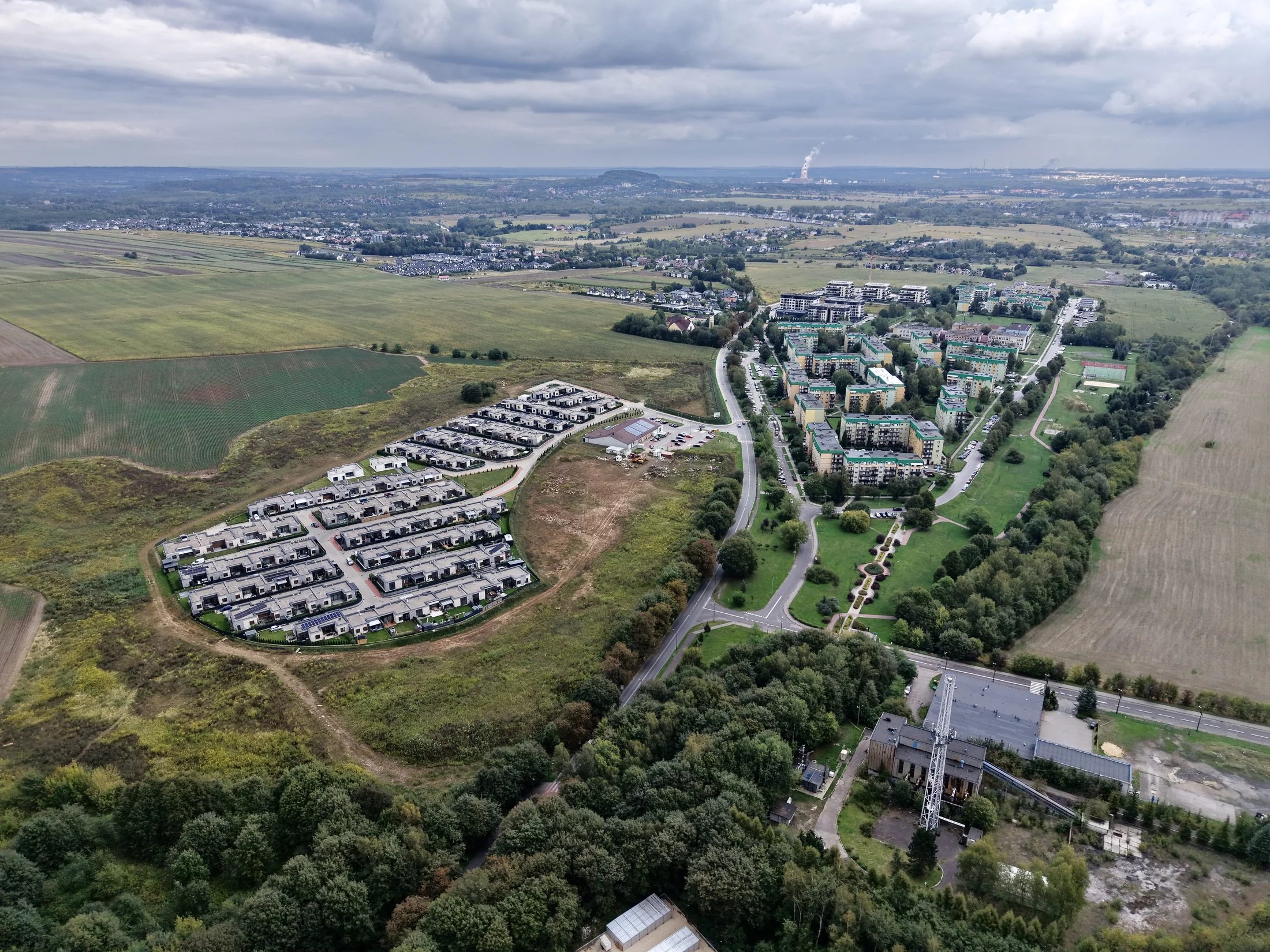 Zabudowa mieszkaniowa i drogi na tle terenów zielonych i otwartych pól.