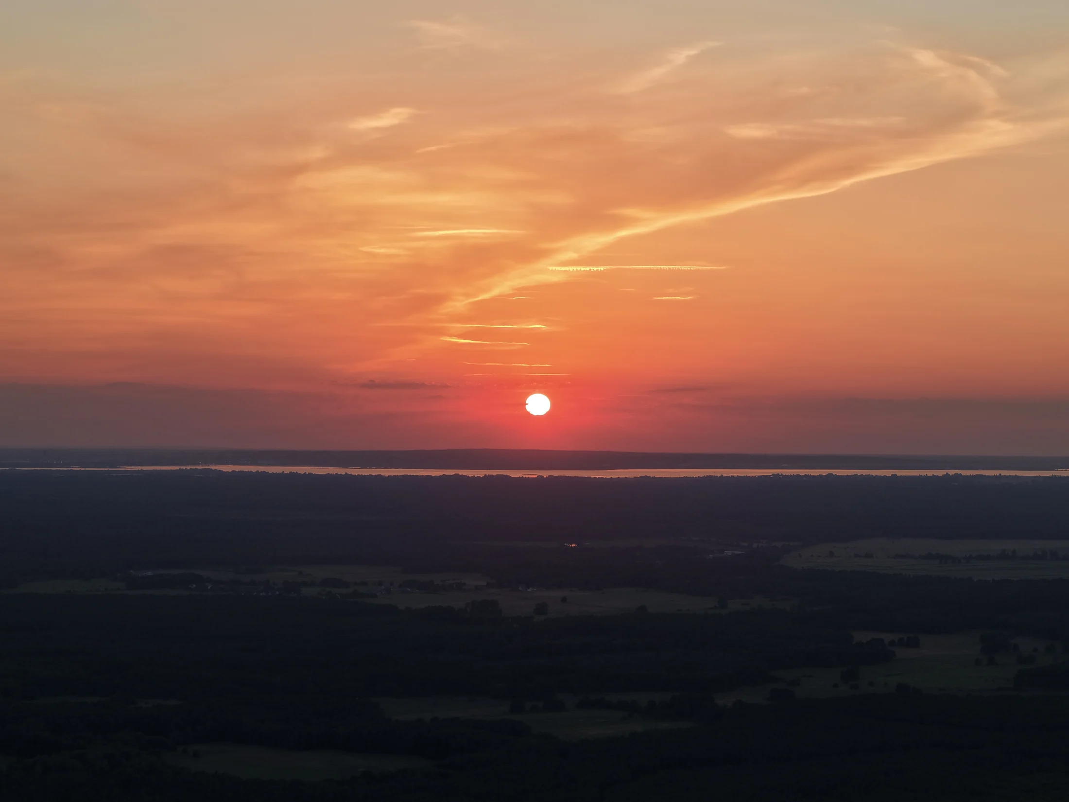 Pomarańczowe słońce i rozświetlone chmury nad ciemnym horyzontem.