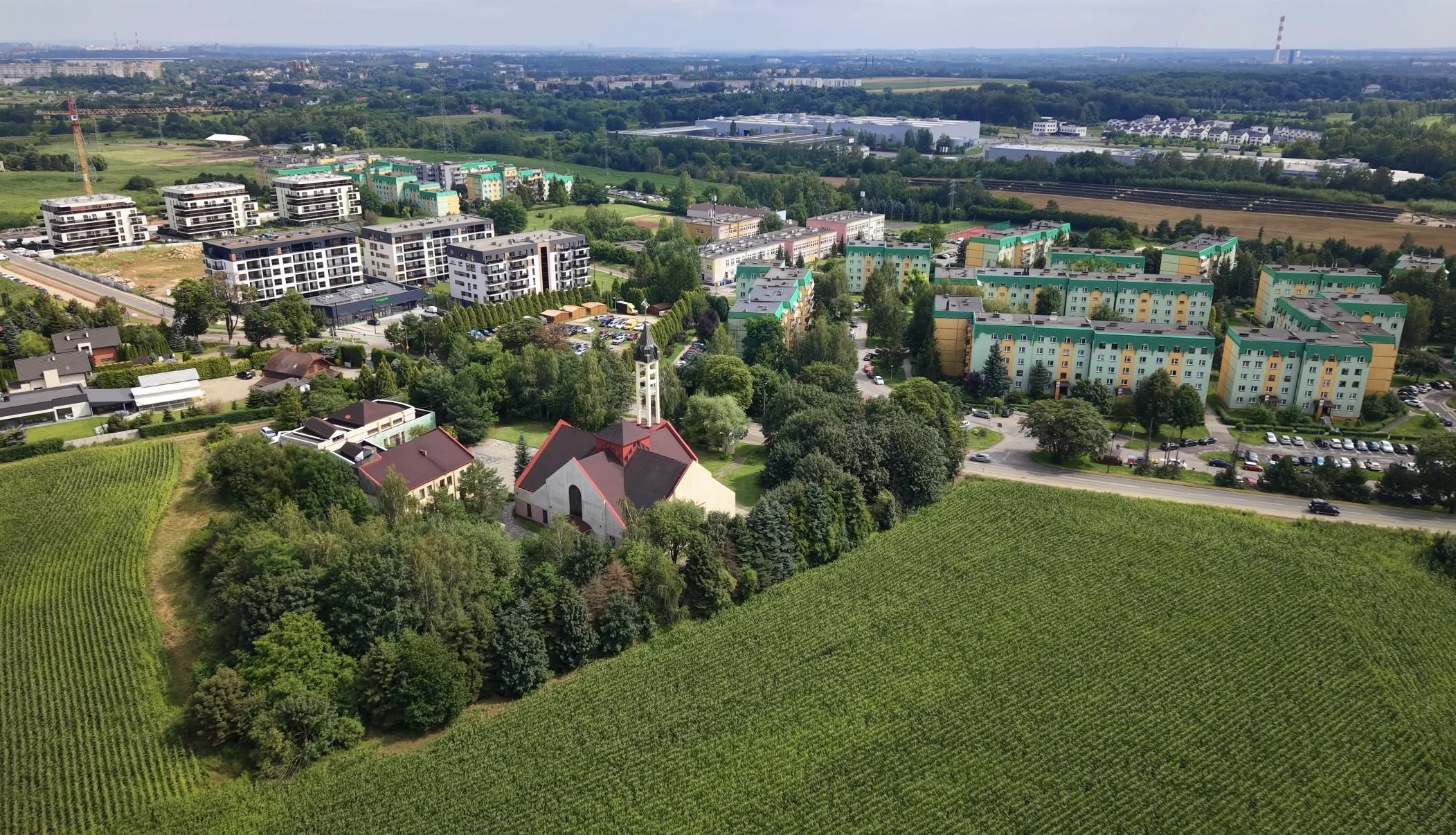 Zabudowa mieszkaniowa, mniejszy budynek i zielone tereny widziane z powietrza.
