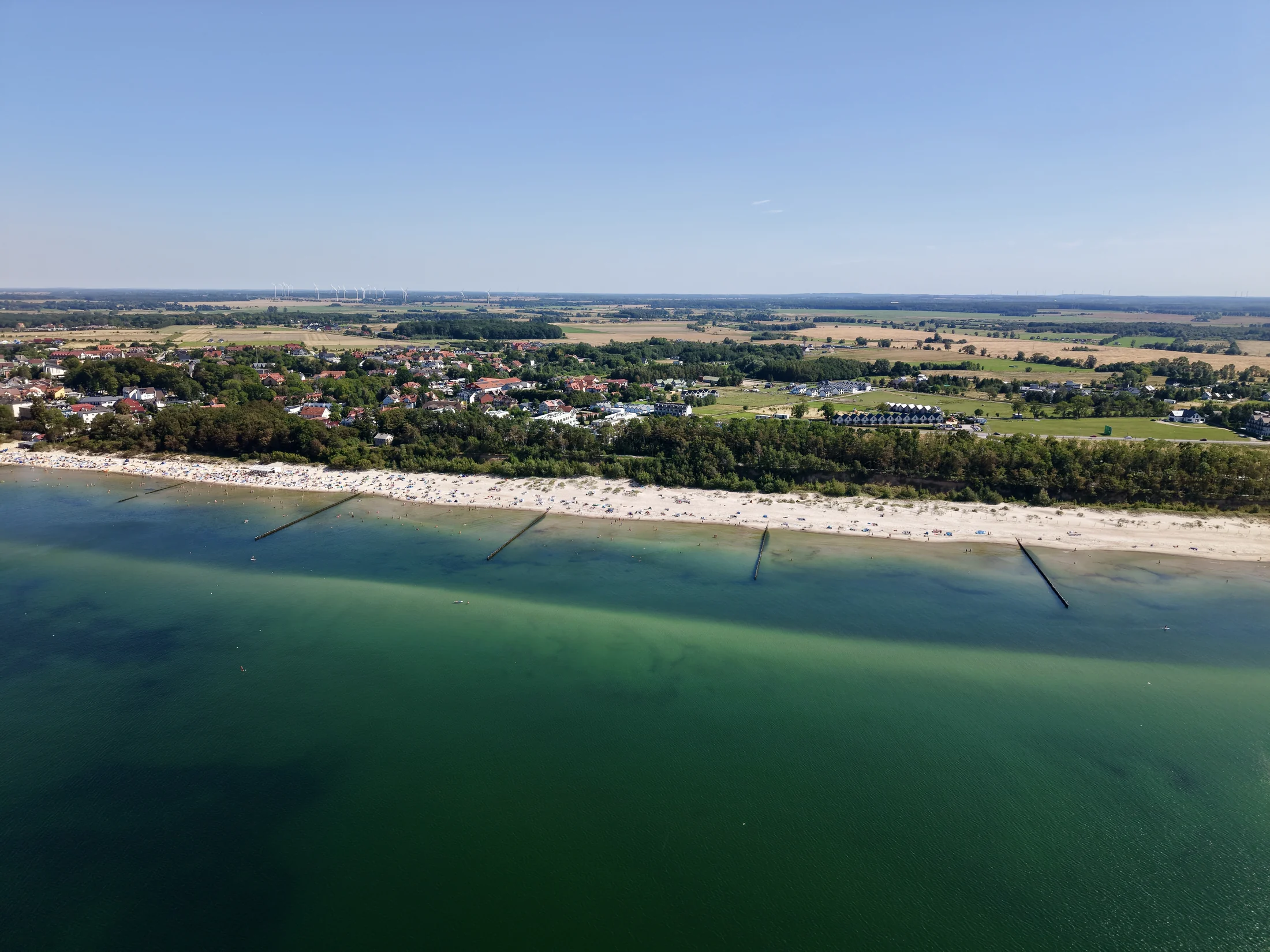 Nadmorska zabudowa, pas plaży i turkusowa woda widziane z powietrza.